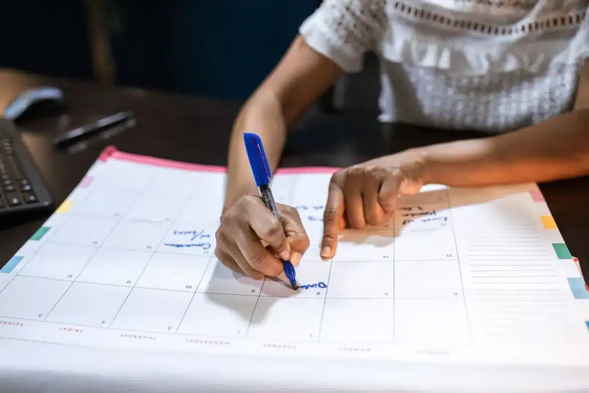 Main marking des jours fériés sur un calendrier mural avec un bloc-notes
