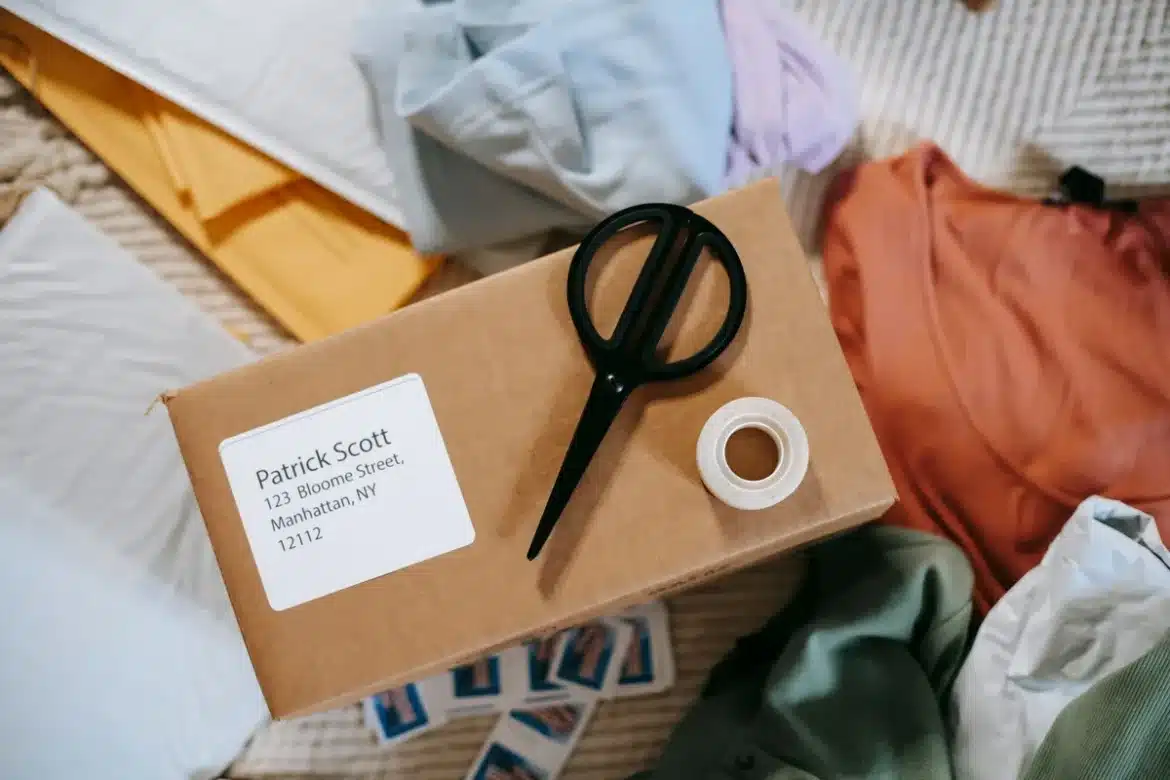 Mains préparant des colis de produits sur un espace de travail avec ordinateur portable et feuille de suivi
