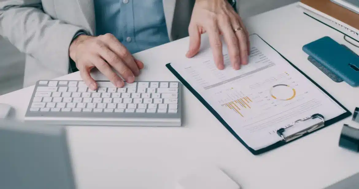 Mains d'une personne organisant des pièces et des documents sur un bureau, avec calculatrice et carnet de notes