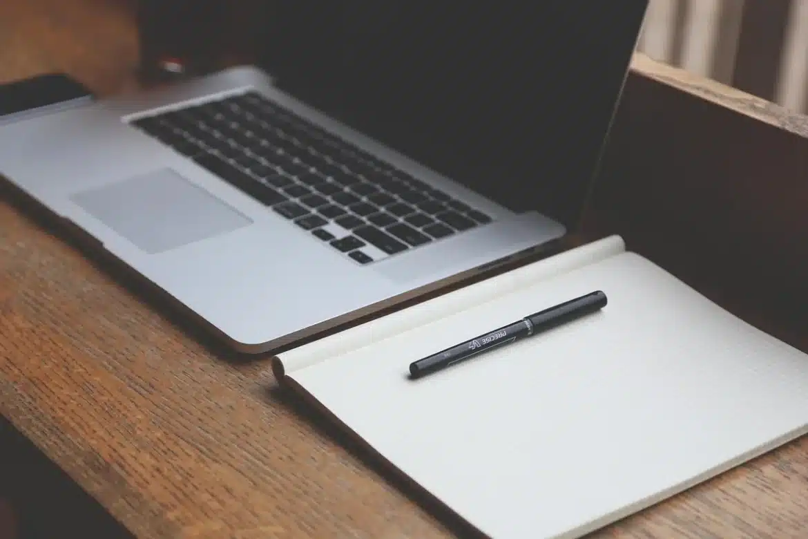 Espace de travail anonyme avec ordinateur portable, carnet et mains tapant